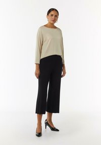 Beige Langarmoberteil, schwarze plissierte weit geschnittene Hose und schwarze spitze High Heels. Das Outfit besteht aus weichen, glatten Stoffen und schafft einen eleganten Look.