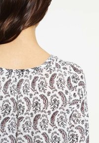 Top in tessuto bianco con motivo paisley rosso e nero, scollatura a giro e dettagli arricciati sul retro.