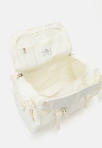 Sac de sport blanc avec un extérieur texturé et des accessoires en métal argenté ; l'intérieur comprend une poche en mesh et un compartiment zippé pour l'organisation.