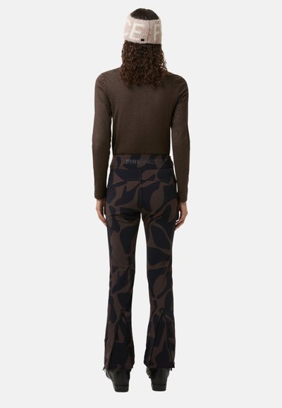 Brown long-sleeve top paired with dark camo-patterned flared pants featuring zippers at the hem. A light-colored headband completes the look.