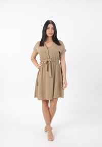 Abito corto beige con scollatura a V, maniche corte, chiusura frontale con bottoni e cintura da annodare. Tessuto morbido con un design fluido.