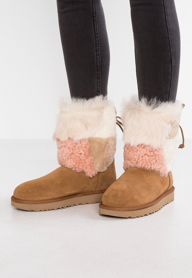 Brązowe zamszowe botki za kostkę z wielokolorowym futrzanym mankietem w odcieniach różu, beżu i kremu. Charakteryzują się teksturowaną powierzchnią i płaską podeszwą.