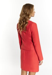 Roter strukturierter Blazer mit passendem Rock; taillierte Passform, lange Ärmel und dezentes geometrisches Muster; glattes Material mit leichtem Glanz.