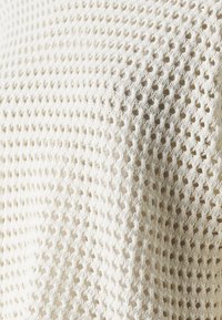 Tessuto bianco a maglia aperta con un motivo geometrico caratterizzato da piccole aperture a forma di diamante; morbido al tatto, leggero e dal design traspirante.