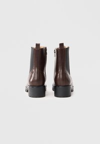 Bottines en cuir brun avec des panneaux latéraux élastiques noirs, présentant un bout rond, une fermeture éclair et des semelles en caoutchouc texturé.