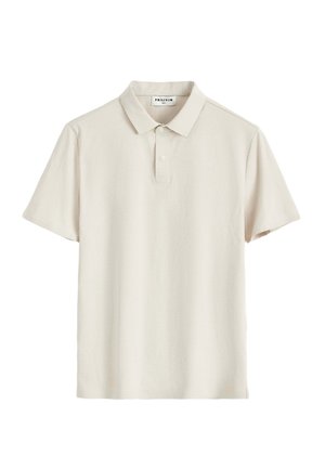 Polo à manches courtes beige clair avec col et patte à deux boutons, présenté à plat avec une étiquette de marque visible à l'intérieur du col.
