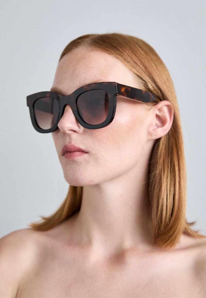 Lunettes de soleil oversize noires et écaille de tortue avec montures angulaires, verres dégradés sombres et branches épaisses. Matériau en plastique lisse.
