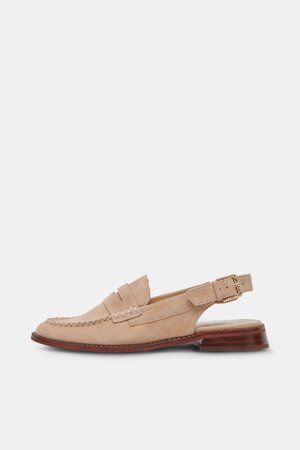 Mocasín de ante beige para mujer con parte trasera abierta, correa con hebilla dorada, detalles cosidos y tacón bajo de madera marrón sobre fondo blanco.