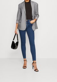 Grå överdimensionerad blazer med rullade ärmar, svart åtsittande skjorta, blå smala jeans, svart blank handväska och svarta klackar med remmar.