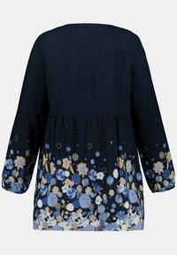 Tmavě navy tunika s dlouhými rukávy, s květinovým vzorem v odstínech modré, krémové a zlaté na lemu, s nařaseným pasem.