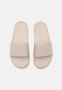 Beige Rutschsandalen mit einem breiten, strukturierten Riemen und glatter Sohle. Hergestellt aus synthetischem Material, zeichnen sie sich durch ein minimalistisches Design aus.