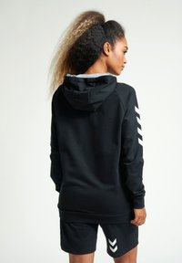 Svart huva sweatshirt med grå foder, med vita chevron detaljer på ärmarna. Matchas med svarta shorts.