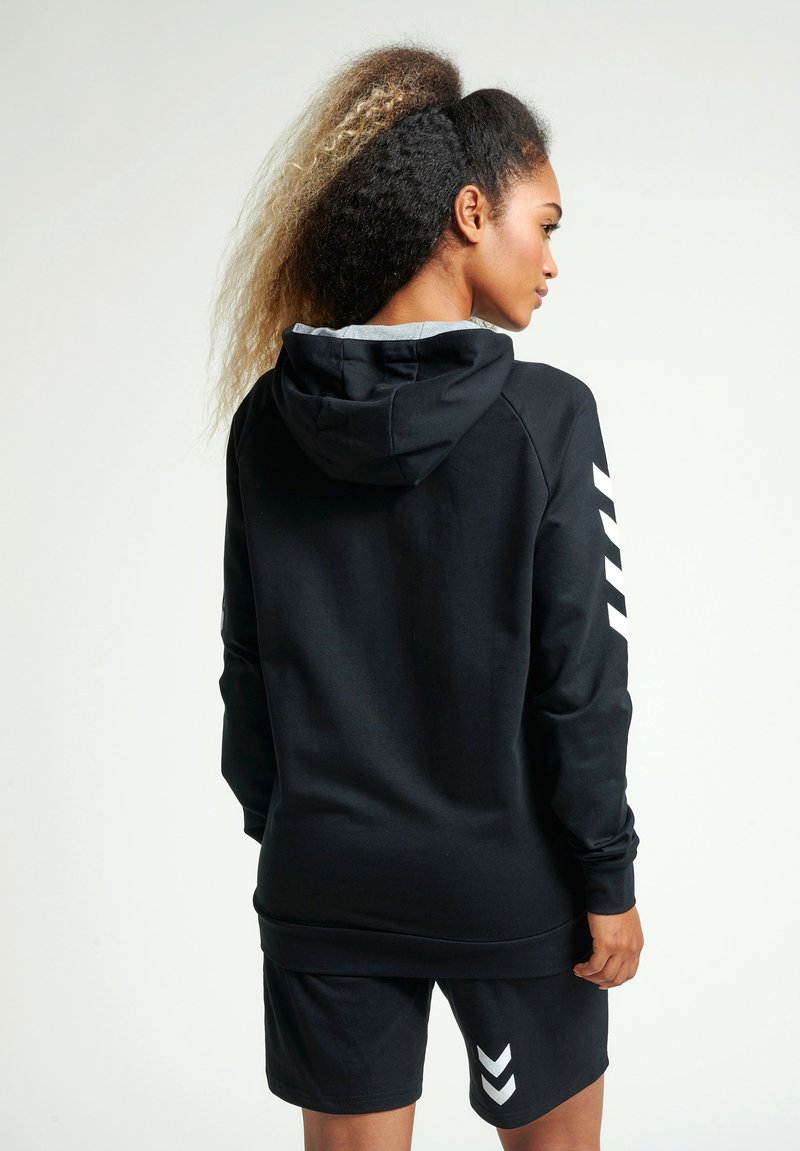 Czarna bluza z kapturem z szarym podbiciem, z białymi akcentami w kształcie chevron na rękawie. Zestawiona z dopasowanymi czarnymi szortami.