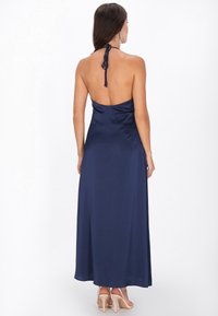 Navy satijnen maxi-jurk met halternek en open rug, met een gladde textuur en een vloeiende silhouet. Minimalistisch ontwerp en enkel-lang.