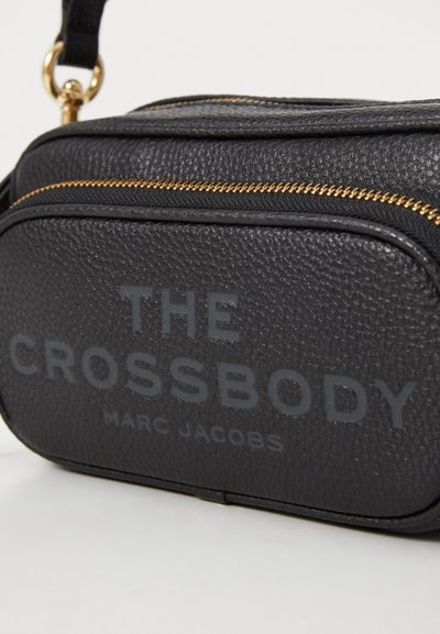 Sort læder crossover taske med guld lynlås. Textureret overflade har "THE CROSSBODY" og "MARC JACOBS" præget i grå. Kompakt rektangulært design.
