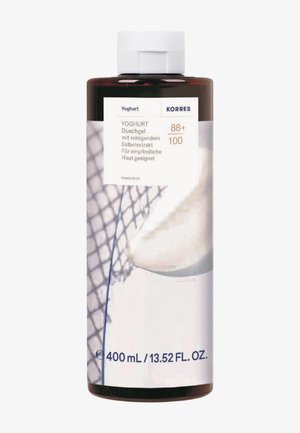 Bottiglia ambra scuro di gel doccia allo yogurt Korres con tappo bianco, etichettata per pelli sensibili, 400 ml, con design di rete e sfondo crema.