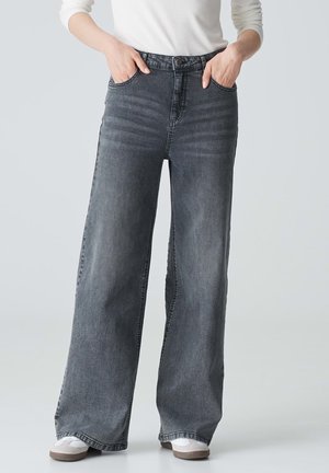 High-waisted wide-leg jeans in dark grey denim with five pockets, visible stitching, and a clean hem. Worn with casual sneakers.