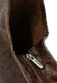 Brązowy, sztuczny but na kostkę w wężowy wzór, wewnętrzna strona z zapięciem na zamek i detalami z hardware RYŁKO. Widoczna miękka tekstura i gładkie wykończenie.