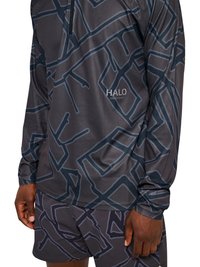 Mężczyzna ubrany w pasującą ciemną koszulkę z długim rękawem i szorty z abstrakcyjnym geometrycznym wzorem oraz napisem "HALO" na piersi koszulki.