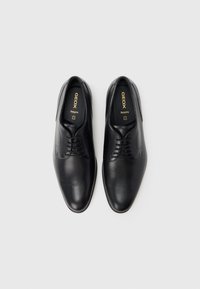 Chaussures à lacets en cuir noir avec une finition lisse, un bout arrondi et un logo embossé sur la semelle intérieure. Design simple et classique avec peu de détails.