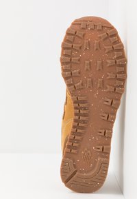 Hnědá gumová podešev boty s hlubokými vzorky, s texturovaným povrchem a tečkami. Na boku je vidět odolný materiál a detail šití.