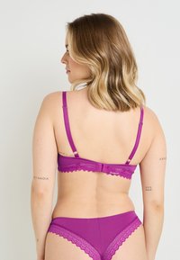 Soutien-gorge violet avec dentelle, doté de bretelles réglables et d'une fermeture à crochet, associé à un bas de bikini assorti avec des accents en dentelle.