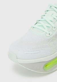 Chaussure de sport vert clair avec un upper en mesh texturé, bout arrondi, fermeture à lacets et une unité de coussinage visible dans le talon.