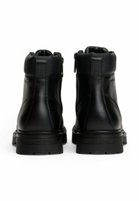 Par de botas de cuero negro hasta el tobillo con suelas gruesas y cuellos acolchados, vistas desde atrás sobre un fondo blanco.