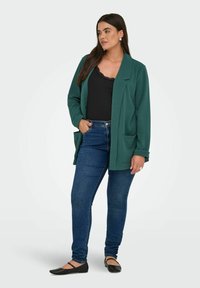 Žalias švarkas su laisvu kirpimu, dviem priekinėmis kišenėmis ir paridenktomis rankovėmis, derinamas su juodu raižytu marškinėliu ir džinsais. Juodi balerinai.