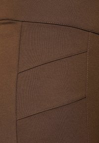 Bruna träningsleggings med en texturerad yta, som har snedställda sömmar och kontrasterande stygn för extra detalj.