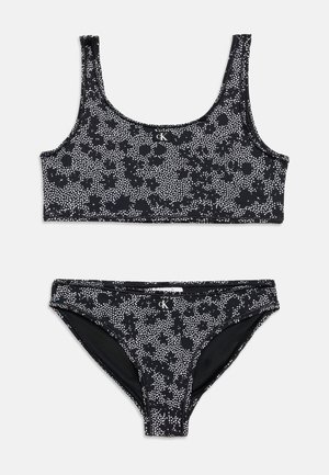 Costum de baie două piese, alb-negru cu pete, cu top cu decolteu rotund și slip bikini cu talie medie, ambele având logo mic CK pe partea din față.