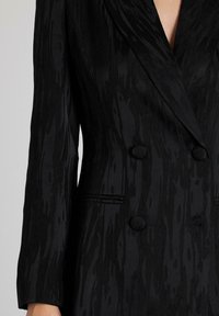 Blazer negro de doble botonadura con tejido texturizado. Presenta solapas con muescas, dos botones redondos y sutiles patrones de rayas verticales.