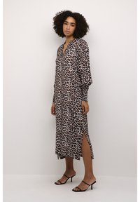 Robe maxi à imprimé léopard avec des manches longues, un décolleté en V profond, des fentes latérales et une silhouette fluide, fabriquée en tissu léger. Sandales à talons noires.