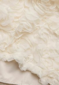 Vit tyg med lager av texturerade blomstermotiv skapar en tredimensionell effekt, som kontrasterar mot en slät bakgrund.