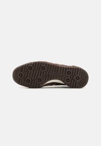 Semelle de sneaker texturée marron avec une semelle extérieure en caoutchouc à motif multidirectionnel. Présente des détails de grip circulaires et un logo embossé.