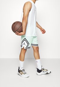 Pánský sportovní outfit s bílým bezrukávovým tričkem, síťovanými šortkami v mátově zelené barvě s černými akcenty a basketbalovými botami se zlatými detaily.