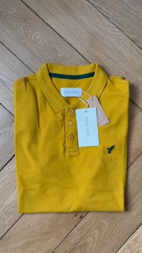 Gelbes Poloshirt aus Baumwolle mit geripptem Kragen, Drei-Knopf-Leiste und kleinem blauen Vogel-Logo auf der linke Brust. Mit Anhängern.