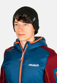 Black ribbed knit beanie worn with a blue and maroon padded jacket featuring orange accents and a logo on the front.