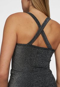 Zwarte glitter stof tanktop met een strakke pasvorm, voorzien van gekruiste bandjes op de rug en een zachte textuur.