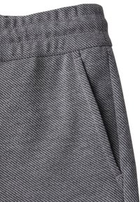 Grå tygbyxor i jogger-stil med ett texturerat hundtandsmönster, elastisk midja och sidofickor. Tyget visar fin detaljrikedom och dimension.