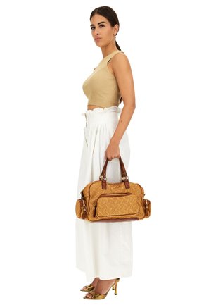 Borsa a tracolla marrone con motivo, manici doppi, tessuto testurizzato e tasche esterne. Abbinata a un top cropped beige e pantaloni bianchi a gamba larga.