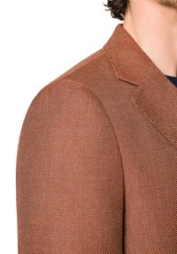 Teksturowana brązowa marynarka z wyraźnym kołnierzem i dopasowanym krojem, ukazująca wysokiej jakości tkany materiał oraz subtelny wzór w jodełkę.