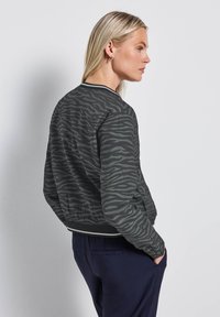 Veste bomber rayée verte et noire avec des poignets et un ourlet côtelés, dotée d'une fermeture éclair et d'une coupe décontractée.