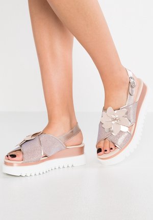 Sandały na koturnie w kolorze metalicznego srebra z teksturowanym wykończeniem, kwiatowym akcentem, otwartymi palcami i białą, żłobioną podeszwą.