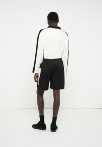 Calções pretos com um cós elástico, combinados com uma camisa de mangas longas branca com riscas laterais pretas. Tecido texturado, design casual.