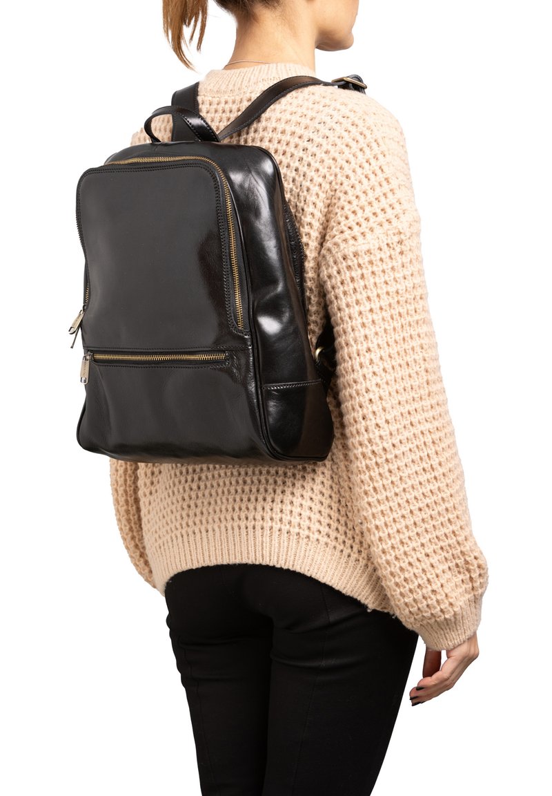 Zaino in pelle nera con finitura liscia, forma rettangolare, due scomparti con zip e spallacci regolabili, indossato sopra un maglione a maglia beige.