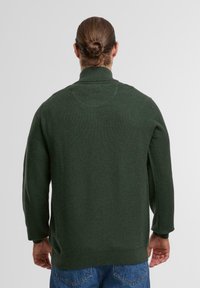 Dunkelgrüner Strickpullover mit hohem Kragen, langen Ärmeln und strukturiertem Finish. Der untere Saum und die Bündchen sind gerippt.