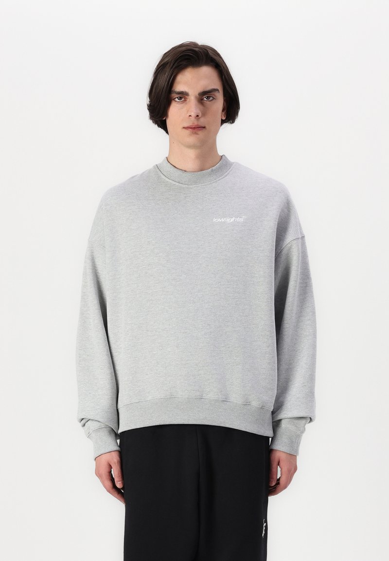 Gray sweatshirt in soft fabric with a crew neck, relaxed fit, and ribbed cuffs. Features a white logo on the left chest. Minimalist design.
