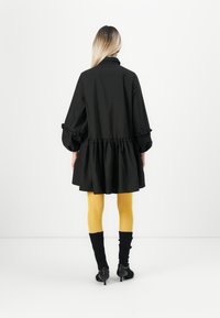 Svart, oversized kjole med puffede ærmer og volangkant, kombinert med gule strømpebukser og svarte ankelstøvler. Ensfarget stoff, minimalistisk design.