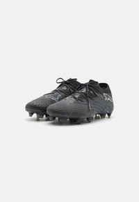 Scarpe da calcio nere con superficie testurizzata, caratterizzate da un design basso, chiusura con lacci e molteplici tacchetti stampati per una migliore trazione.